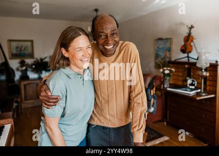 Porträt eines glücklichen älteren Mannes, der mit Arm um eine Krankenschwester im Wohnzimmer zu Hause steht Stockfoto