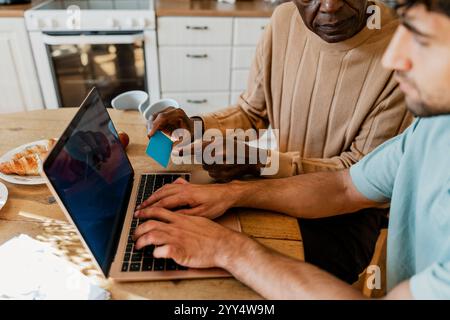 Junge männliche Krankenschwester mit Laptop von einem älteren Mann mit Kreditkarte zu Hause Stockfoto