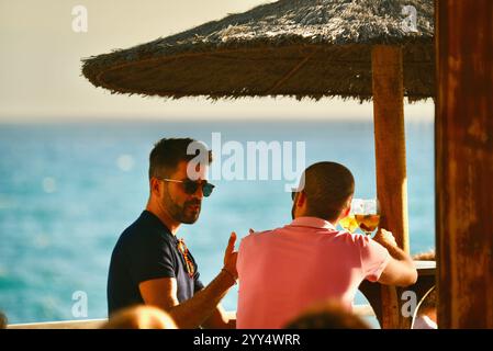 Zwei junge Männer genießen Bier und unterhalten sich in einem Außenbereich am Meer, am Formosa Beach, der tropischen Insel Madeira, Portugal Stockfoto