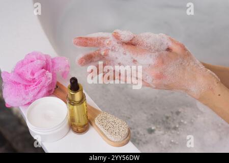 Frau, die Duschgel auf die Hand im Innenbad aufträgt, Nahaufnahme auf dem Hintergrund des Badezimmers, Körper- und Haarpflegeprodukte in der Nähe Stockfoto