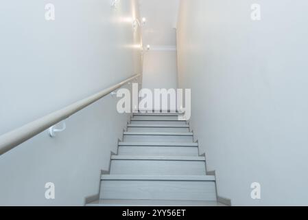 Hell beleuchtete Treppe mit Holztreppen und minimalistischem Handlauf in einem modernen, sauberen und einfachen Haus. Die Wände sind schlicht und weiß, was ein offenes Licht schafft Stockfoto