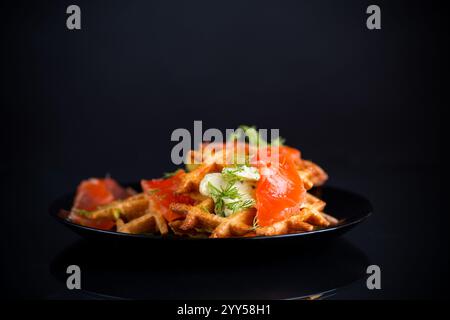 Gemüskartoffelwaffeln mit Aufstrich und leicht gesalzenem rotem Fisch auf einem Teller, isoliert auf schwarzem Hintergrund. Stockfoto