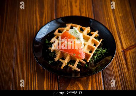 Gemüskartoffelwaffeln mit Aufstrich und leicht gesalzenem rotem Fisch, auf einem Teller auf einem Holztisch. Stockfoto