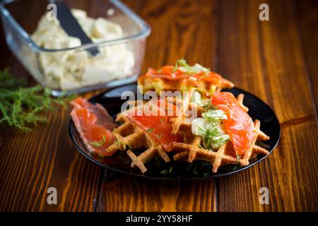 Gemüskartoffelwaffeln mit Aufstrich und leicht gesalzenem rotem Fisch, auf einem Teller auf einem Holztisch. Stockfoto