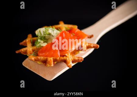 Gemüskartoffelwaffeln mit Aufstrich und leicht gesalzenem rotem Fisch auf einem Spachtel, isoliert auf schwarzem Hintergrund Stockfoto