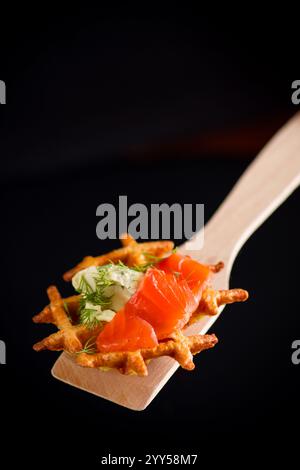 Gemüskartoffelwaffeln mit Aufstrich und leicht gesalzenem rotem Fisch auf einem Spachtel, isoliert auf schwarzem Hintergrund Stockfoto