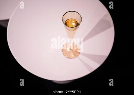 Ein luxuriöses goldenes Glas mit prickelndem Champagner auf weißem runden Tisch vor schwarzem Hintergrund. Stockfoto