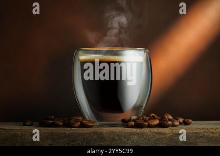 Heißer Espresso in Glasbecher Espresso mit Bohnen auf Holztisch mit braunem Hintergrund Stockfoto