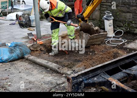 Arbeiter graben ein Loch, um die Leitung freizulegen, und Schaufeln in Baggerlöffel auf dem Asphalt während Bauarbeiten Stockfoto