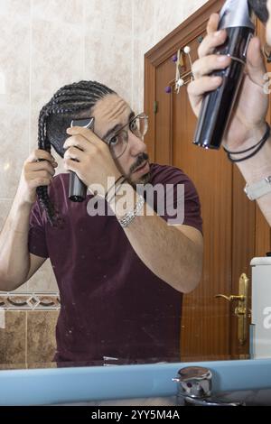 Ein Mann schneidet sich im Badezimmer mit einem Haarschneider die Haare. Nahaufnahme eines Mannes, der sich im Badezimmer mit einem Haarschneider die Haare schneidet Stockfoto