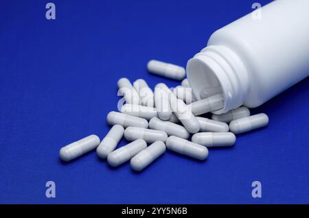 Große weiße Pillen fielen aus einer großen weißen Flasche. Leben ohne Drogen und Abhängigkeit von Kapseln mit Antibiotika, Medizin, Amphetaminen, Medikamenten und Medikamenten Stockfoto
