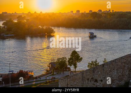 Die Sonne untergeht über dem Fluss Save und wirft goldene Farbtöne über das Wasser. Von der Kalamegdan-Festung in Belgrad aus bietet sich der Blick auf die friedliche Natur und die Skyline der Stadt, die sich wunderbar verschmelzen. Stockfoto