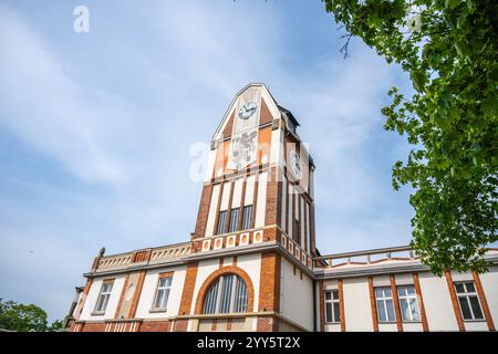 Das Wasserkraftwerk Hucak in Hradec Kralove zeigt ein atemberaubendes Jugendstildesign mit einem markanten Uhrenturm und komplizierten Ziegelmauern vor einem klaren blauen Himmel. Stockfoto