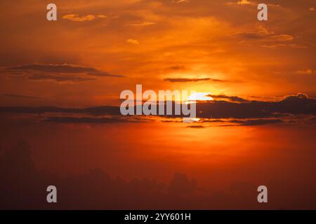 Ein Blick auf die untergehende Sonne am Himmel, teilweise versteckt hinter Wolkenschichten. Intensive Orange-, Rot- und Goldtöne. Eine Idee für einen Hintergrund oder eine Wa Stockfoto