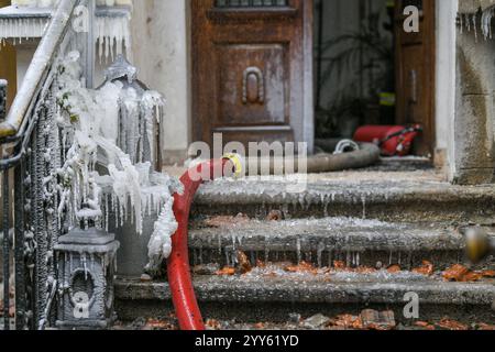 Ein gerissener Feuerschlauch führt Wasser aus, wodurch Eis und Eiswürfel um die Treppen und Zäune aus einem brennenden Haus entstehen. Ruß ist überall vorhanden. Stockfoto