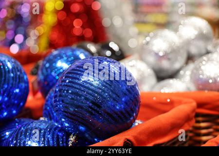 Weihnachtsspielzeug, blaue Kugeln im roten Korb auf verschwommenem festlichem Lichthintergrund. Neujahrsdekoration in einem Laden Stockfoto