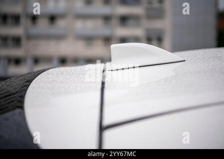 Nahaufnahme: Weiße GPS-Antenne in Form einer Haifischflosse auf dem Dach des Fahrzeugs für das Radio-Navigationssystem. Antennenhai-Flosse auf verschwommenem Hintergrund mit Regentropfen. Stockfoto