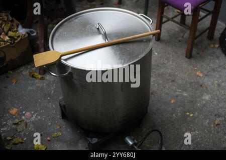 Großer Aluminiumtopf mit Gasflasche in der Campingküche. Herstellung von Traiditionsnahrung im Metallkessel. Großer Holzlöffel auf dem Topf. Stockfoto