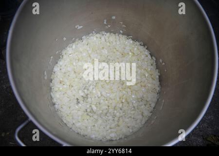 Rösten der zerkleinerten weißen Zwiebeln in einem großen Aluminiumtopf mit Gasflasche in der Campingküche. Zubereitung traditioneller Speisen im Metallkessel. Nahaufnahme. Stockfoto