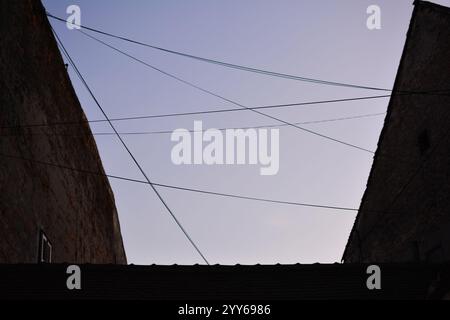 Elektrische Leitungen verlaufen zwischen zwei alten Ziegelgebäuden. Himmel im Hintergrund. Gebäude auf dem Dach. Stockfoto