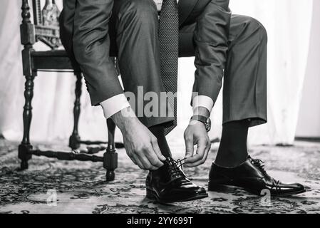 Ein Geschäftsmann bindet Schnürsenkel an Schuhe in der Nähe. Herrenhände und ein Paar Lederschuhe. Geschäftsmännermorgen. Schwarz-weiß-Foto, der Bräutigam. Stockfoto