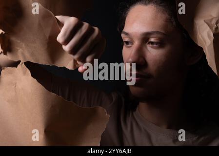 Ein junger Mann, der durch ein Loch in einem Blatt braunem Papier rauskommt. Nahaufnahme. Studio-Porträt. Stockfoto