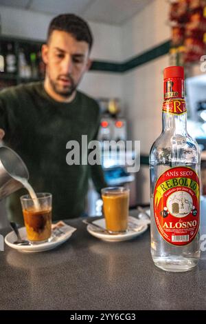 Alosno, Spanien, 14. Dezember 2024, Szene eines Barkepers, der Kaffee und Spirituosen mit einer Spirituosenflasche serviert. Stockfoto