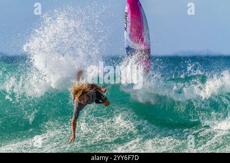 Ein Surfer, der in dem entscheidenden Moment gefangen war, als er sein Board durch eine rote Welle von den Felsen verlor. Stockfoto