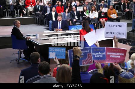 Moskau, Russland. Dezember 2024. Der russische Präsident Wladimir Putin hört eine Frage mit den Gastgebern Alexandra Suworova, Linke, und Dmitri Kulko, Zentrum, während der jährlichen Pressekonferenz und Call-in-Show in Gostinny Dvor, 19. Dezember 2024 in Moskau, Russland. Quelle: Vyacheslav Prokofyev/Kreml Pool/Alamy Live News Stockfoto