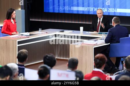 Moskau, Russland. Dezember 2024. Der russische Präsident Wladimir Putin, Mitte, antwortet auf eine Frage mit den Gastgebern Alexandra Suworova, links, und Dmitri Kulko, rechts, während der jährlichen Pressekonferenz und Call-in-Show in Gostinny Dvor, 19. Dezember 2024 in Moskau. Quelle: Gavriil Grigorov/Kreml Pool/Alamy Live News Stockfoto