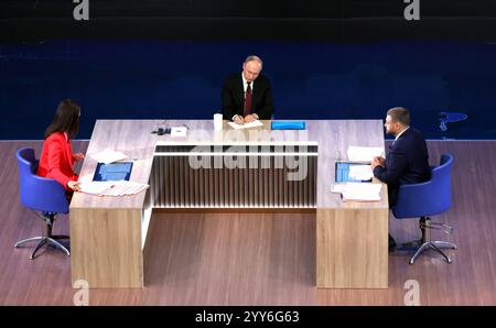 Moskau, Russland. Dezember 2024. Der russische Präsident Wladimir Putin, Mitte, hört eine Frage mit den Gastgebern Alexandra Suworova, links, und Dmitri Kulko, rechts, während der jährlichen Pressekonferenz und Call-in-Show in Gostinny Dvor, 19. Dezember 2024 in Moskau, Russland. Quelle: Vyacheslav Prokofyev/Kreml Pool/Alamy Live News Stockfoto