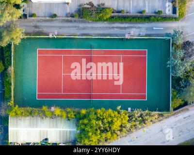 Blick aus der Vogelperspektive auf einen lebhaften rot-grünen Tennisplatz, umgeben von Bäumen und Gebäuden. Stockfoto
