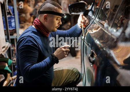 Mann repariert das Fahrzeug in der Werkstatt mit Scheinwerfer, der auf die Detaillierung fokussiert ist. Stockfoto