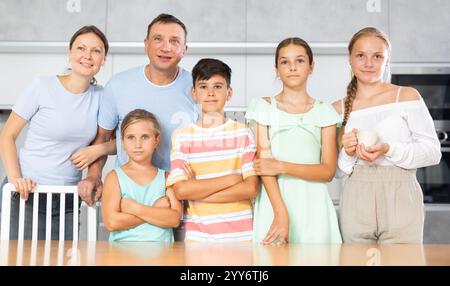 Glücklicher Vater und Mutter mit drei Töchtern und Sohn stehen neben dem Küchentisch. Stockfoto
