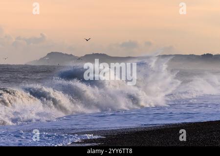 An einem kalten Wintermorgen an der Ostküste von Norfolk im Dezember krachen Flut-Wellen gegen den Kieselstrand von Cley Next Sea. Stockfoto