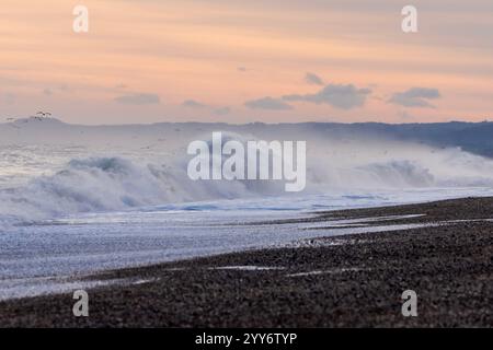 An einem kalten Wintermorgen an der Ostküste von Norfolk im Dezember krachen Flut-Wellen gegen den Kieselstrand von Cley Next Sea. Stockfoto