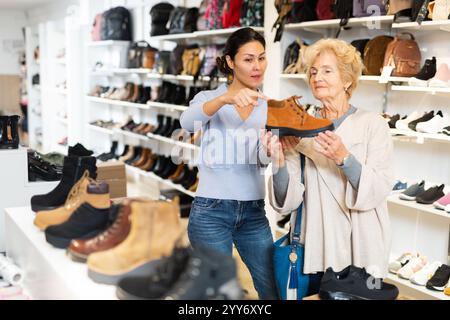 Verkäuferin hilft Oma bei der Auswahl neuer Schuhe Stockfoto