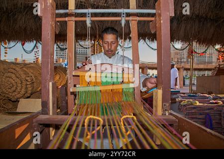 Ein arabischer Handwerker, der während des 14. Traditionellen Dhow-Festivals in Katara in Doha, Katar, an traditionellen Holzwebstühlen mit farbigen Fäden arbeitet Stockfoto