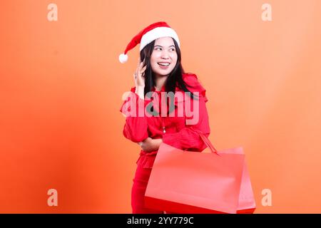 Ausdruck von erwachsenen Frauen mit weihnachtskleid, weihnachtsmütze, glücklich mit der linken Hand, Haare und tragen rote Tasche mit weihnachtsgeschenken, isoliert auf Stockfoto