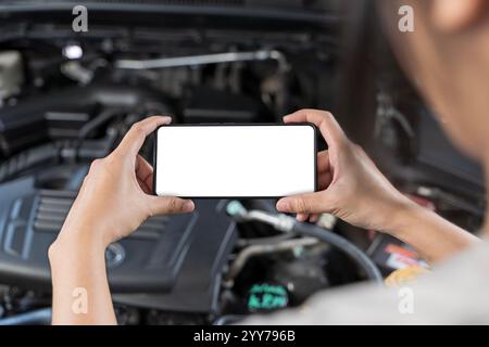 Nahaufnahme von Frauenhänden, die das Smartphone halten, mit leerem Platz auf dem Bildschirm für Ihren Text, Hintergrund des Motors, in der Nähe einer geöffneten Motorhaube, die den Motor zeigt Stockfoto