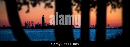 Chantry Island Lighthouse, umrahmt von Silhouettenbäumen bei Sonnenuntergang, mit leuchtenden Orange- und Blautönen, die sich über dem Wasser spiegeln, Southampton, IN Kanada Stockfoto