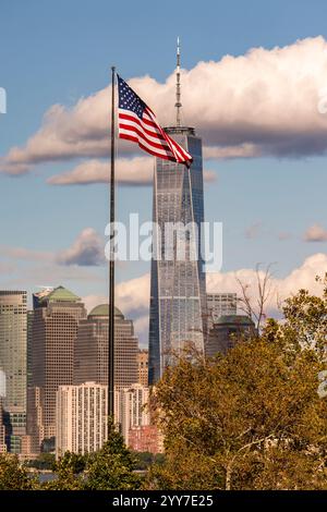 One World Trade Center fotografiert von Liberty Island mit der ikonischen US-Flagge vor der Kamera. Stockfoto