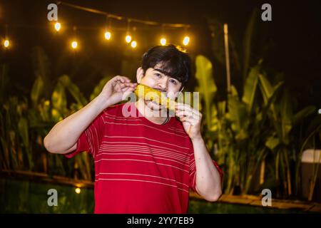 Ein Mann Lächelt, Während Er Gerösteten Mais Isst. Mann genießt gerösteten Mais draußen in der Nacht. Stockfoto