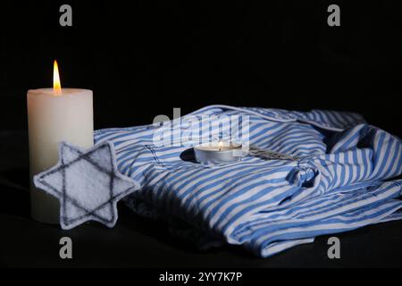 Brennende Kerzen mit jüdischem Abzeichen und Gefangenenuniform auf dunklem Hintergrund. Internationaler Holocaust-Gedenktag Stockfoto