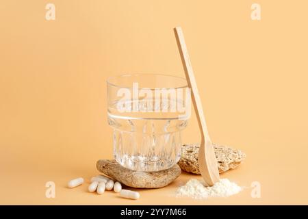 Glas Wasser mit Holzlöffel, Kollagenpulver und Pillen auf beigefarbenem Hintergrund Stockfoto