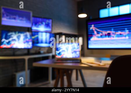 Verschwommene Sicht auf Laptop- und Computermonitore mit Bestandsdaten auf Tischen im Büro des Händlers bei Nacht Stockfoto