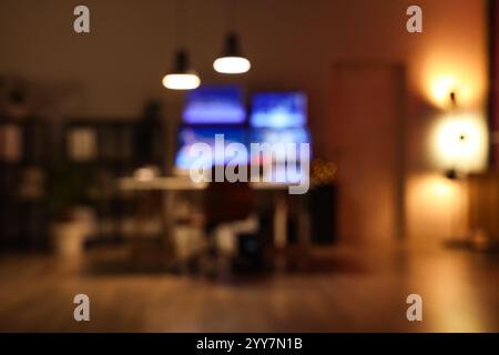 Verschwommener Blick auf das dunkle Büro mit dem Arbeitsplatz des Händlers und leuchtenden Lampen bei Nacht Stockfoto