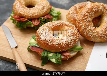 Holzbrett mit leckeren Bagel-Sandwiches mit Zutaten auf schwarzem Hintergrund Stockfoto