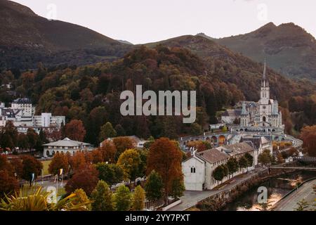 Lourdes Wahrzeichen im Abendhimmel. Kathedrale unserer Lieben Frau von Lourdes mit Fluss und Bergen. Berühmtes Pilgerzentrum. Rosenkranzheiligtum in Lourdes Stockfoto