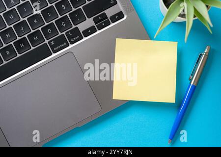 Draufsicht des leeren Post-it-Dokuments, das auf dem Laptop auf dem blauen Tisch feststeckt Stockfoto